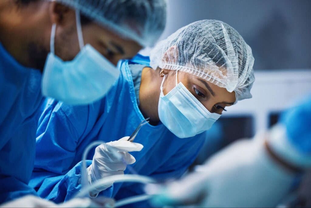 A male and female surgeon lean over a patient with hairnets and masks on.