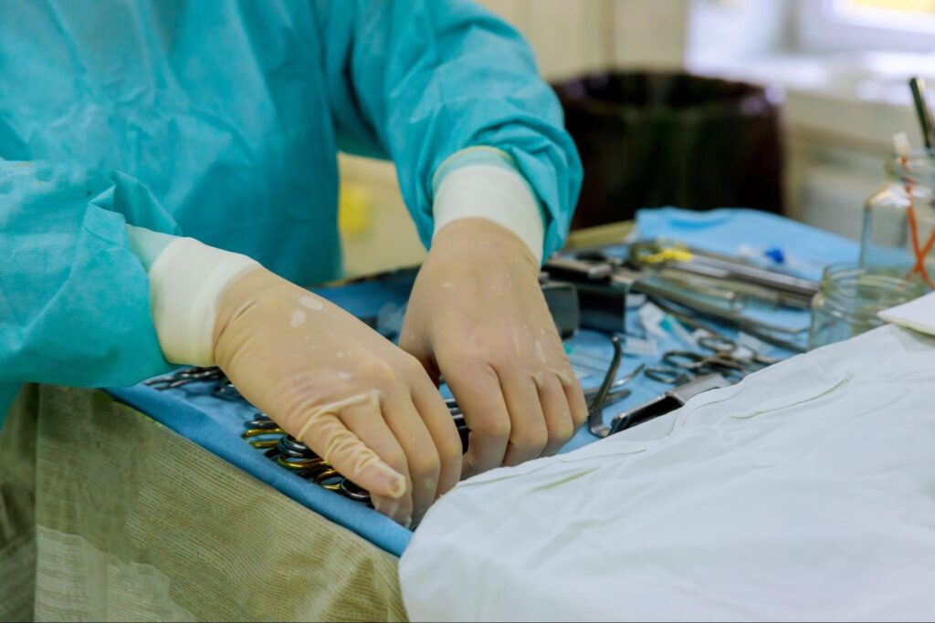 Surgeon with gloves holding metal instruments and tools.